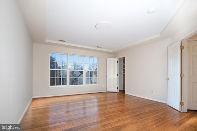 spare room with a raised ceiling and light hardwood / wood-style flooring