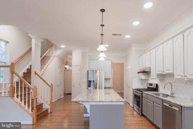 kitchen featuring pendant lighting, sink, white cabinetry, stainless steel appliances, and a center island