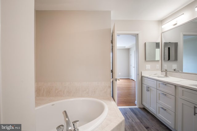 bathroom featuring a relaxing tiled tub, wood-type flooring, and vanity