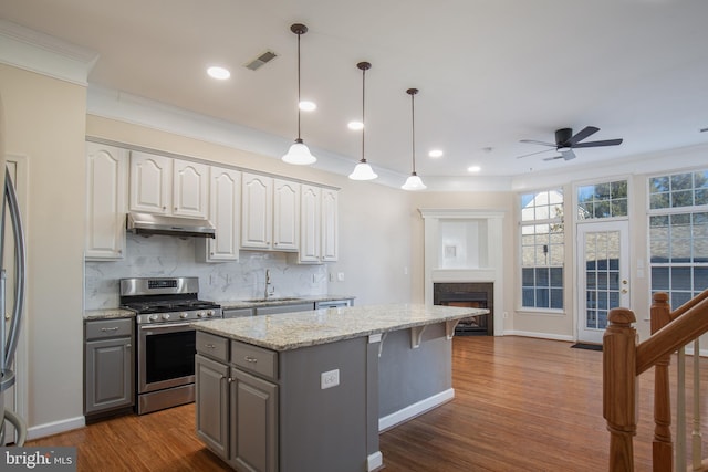 kitchen featuring pendant lighting, gray cabinetry, a center island, light stone countertops, and gas range