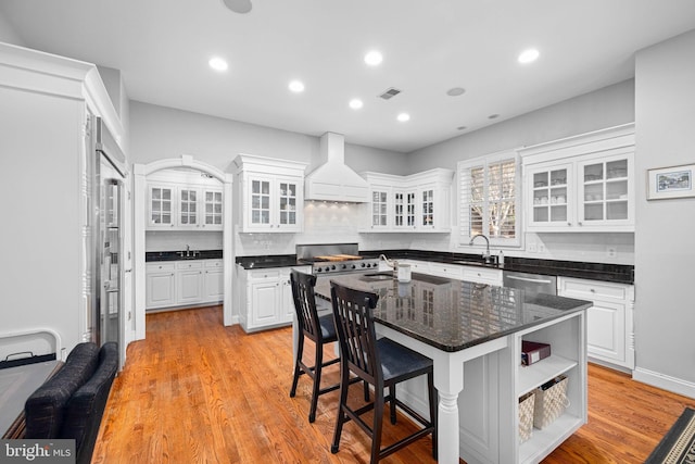 kitchen featuring a breakfast bar area, premium range hood, white cabinetry, a center island, and light hardwood / wood-style floors