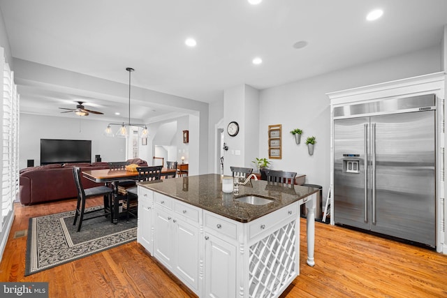 kitchen with sink, built in refrigerator, dark stone counters, a kitchen island with sink, and white cabinets