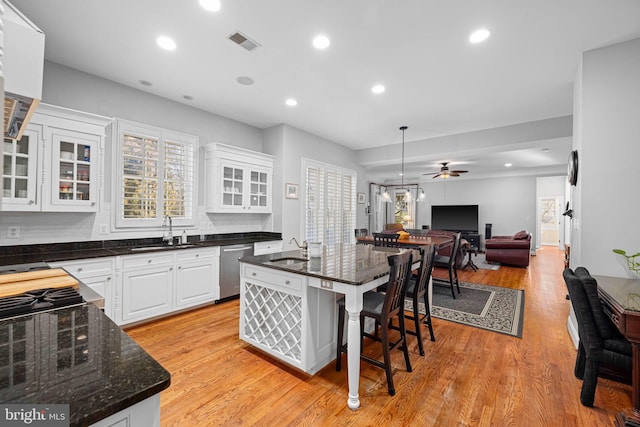 kitchen with sink, hanging light fixtures, a kitchen breakfast bar, a kitchen island with sink, and white cabinets