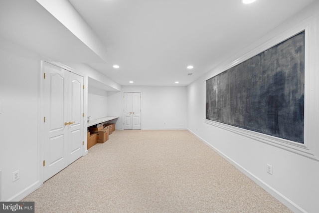 basement featuring light colored carpet and built in desk