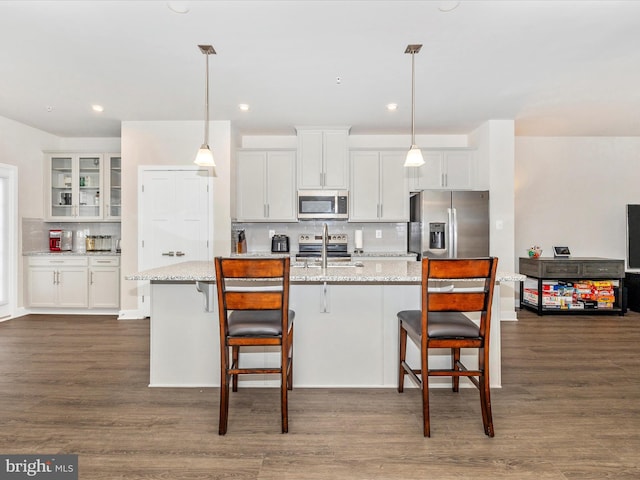 kitchen featuring pendant lighting, light stone countertops, stainless steel appliances, and white cabinets