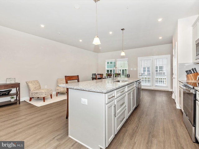 kitchen with appliances with stainless steel finishes, sink, hanging light fixtures, light stone counters, and a center island with sink