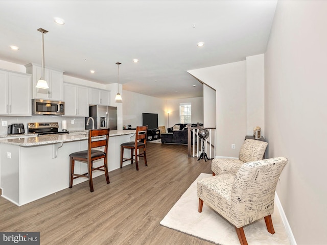 kitchen featuring appliances with stainless steel finishes, white cabinetry, a kitchen bar, hanging light fixtures, and light stone countertops