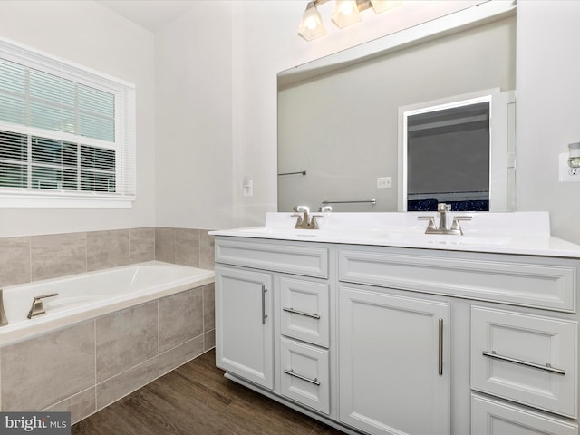 bathroom featuring a relaxing tiled tub, vanity, and wood-type flooring