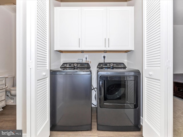 clothes washing area featuring light hardwood / wood-style floors, cabinets, and washing machine and clothes dryer