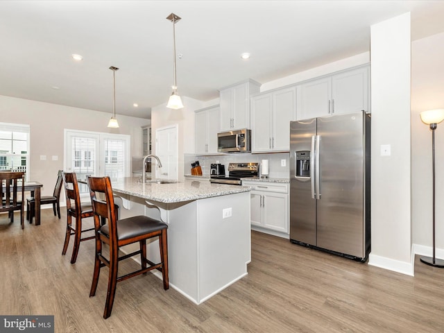 kitchen with white cabinetry, stainless steel appliances, sink, and a center island with sink