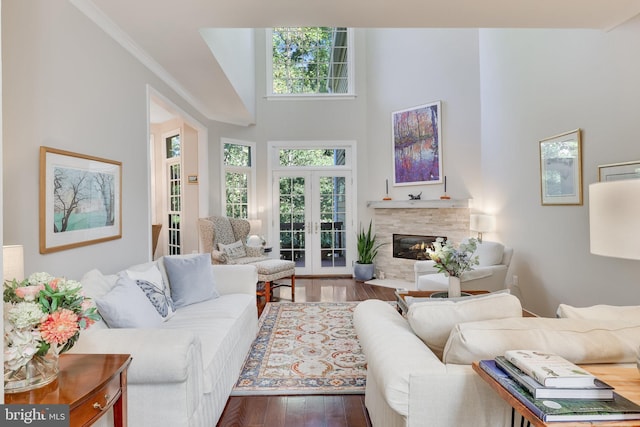 living room featuring crown molding, a towering ceiling, wood-type flooring, a tiled fireplace, and french doors