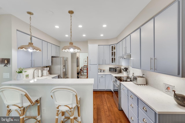 kitchen with pendant lighting, a kitchen breakfast bar, stainless steel appliances, dark hardwood / wood-style flooring, and kitchen peninsula