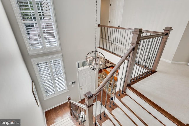 stairway with an inviting chandelier, a towering ceiling, a healthy amount of sunlight, and hardwood / wood-style floors