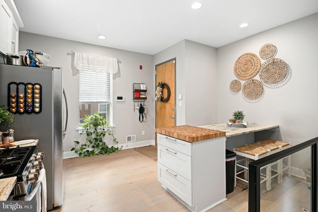 kitchen with white cabinetry, butcher block counters, gas range, and light hardwood / wood-style flooring