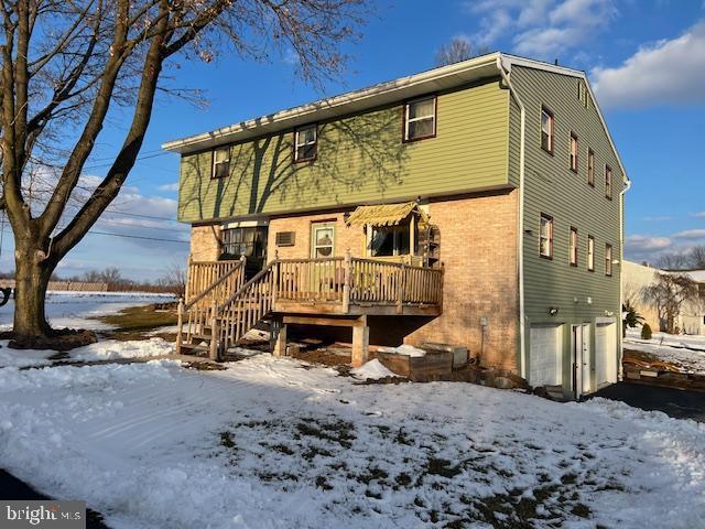 snow covered rear of property with a garage and a deck