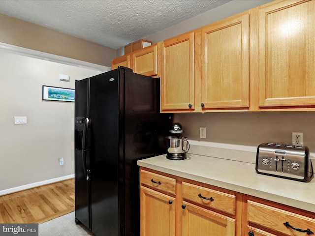 kitchen with light brown cabinetry, black fridge with ice dispenser, a textured ceiling, and light wood-type flooring