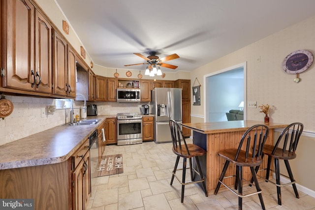 kitchen featuring sink, backsplash, a kitchen breakfast bar, ceiling fan, and stainless steel appliances