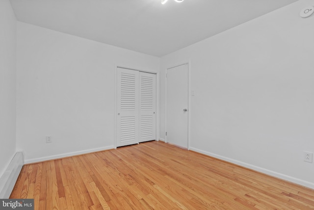 unfurnished bedroom featuring a baseboard heating unit, light hardwood / wood-style floors, and a closet