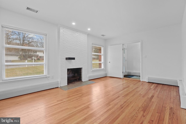 unfurnished living room with a baseboard heating unit, a fireplace, and light hardwood / wood-style flooring