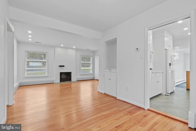 unfurnished living room with a baseboard heating unit, a fireplace, and light wood-type flooring