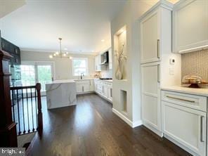 kitchen with pendant lighting, tasteful backsplash, white cabinets, dark hardwood / wood-style flooring, and a chandelier