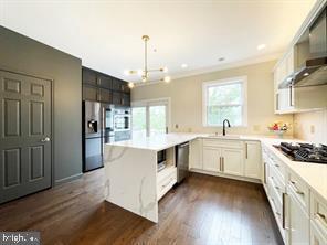 kitchen with white cabinetry, stainless steel appliances, dark hardwood / wood-style flooring, decorative light fixtures, and wall chimney exhaust hood