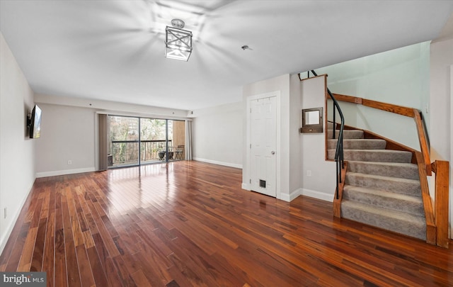 unfurnished living room with stairway, wood finished floors, and baseboards