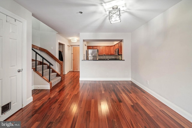 unfurnished living room featuring dark wood-style flooring, visible vents, stairway, and baseboards