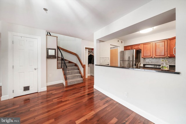 kitchen with tasteful backsplash, dark countertops, brown cabinets, dark wood-type flooring, and freestanding refrigerator