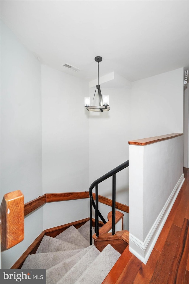 staircase with a chandelier, visible vents, baseboards, and wood finished floors