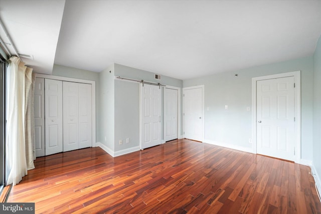 unfurnished bedroom with two closets, visible vents, a barn door, wood finished floors, and baseboards