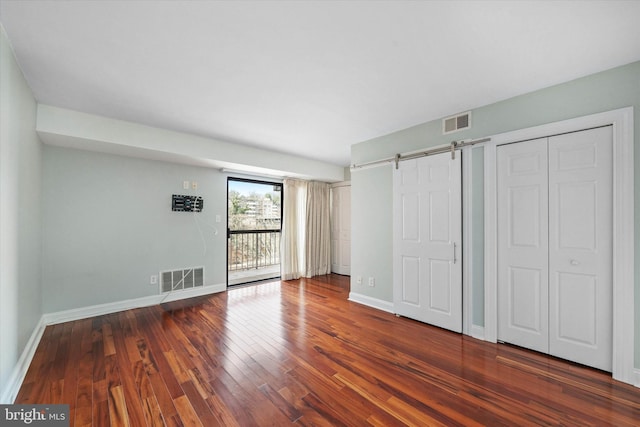 unfurnished bedroom featuring baseboards, a barn door, visible vents, and wood finished floors