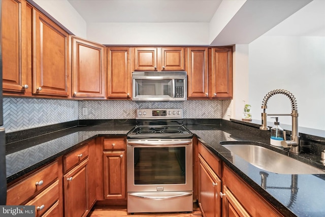 kitchen with stainless steel appliances, dark stone counters, brown cabinetry, and a sink