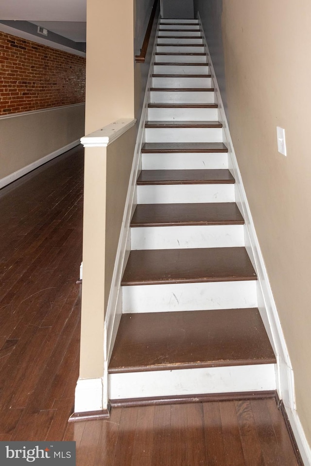 stairs featuring hardwood / wood-style flooring and brick wall