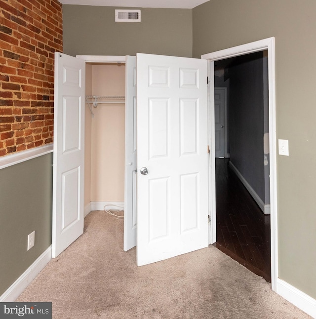 unfurnished bedroom featuring brick wall, carpet floors, and a closet