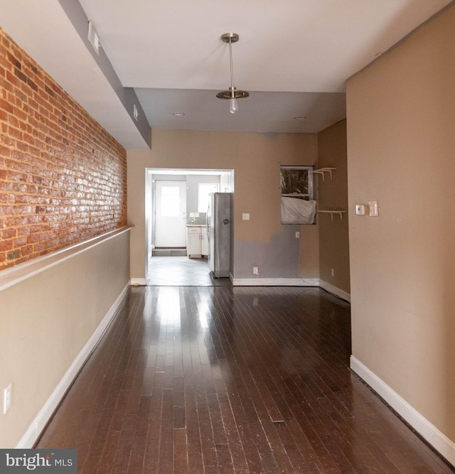 unfurnished living room with brick wall and dark hardwood / wood-style floors