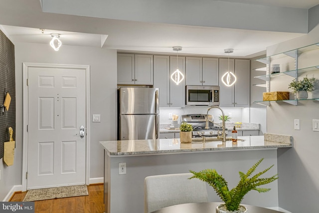 kitchen with appliances with stainless steel finishes, decorative light fixtures, backsplash, light stone counters, and kitchen peninsula