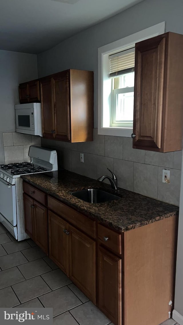 kitchen with sink, white appliances, dark stone countertops, tasteful backsplash, and light tile patterned flooring