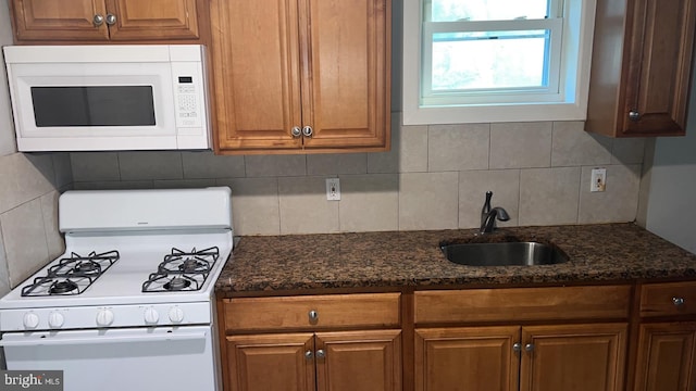 kitchen with tasteful backsplash, white appliances, sink, and dark stone countertops