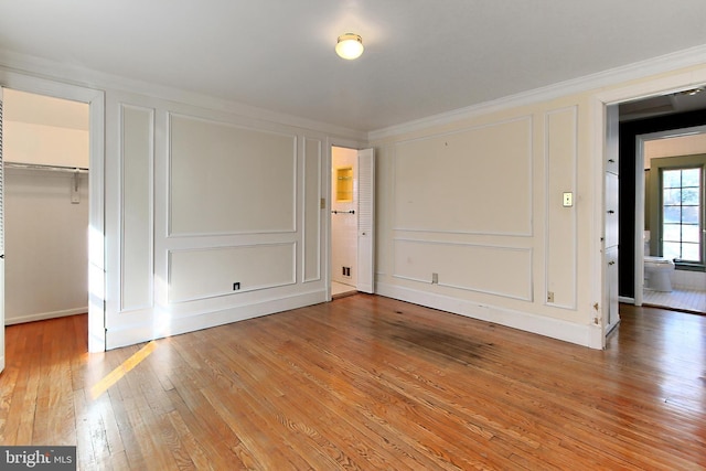 unfurnished bedroom with ornamental molding, a spacious closet, light hardwood / wood-style floors, and a closet