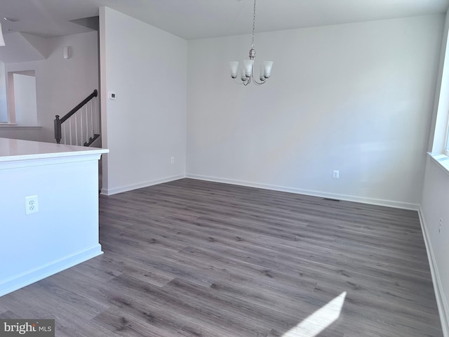 spare room featuring dark wood-type flooring and a notable chandelier