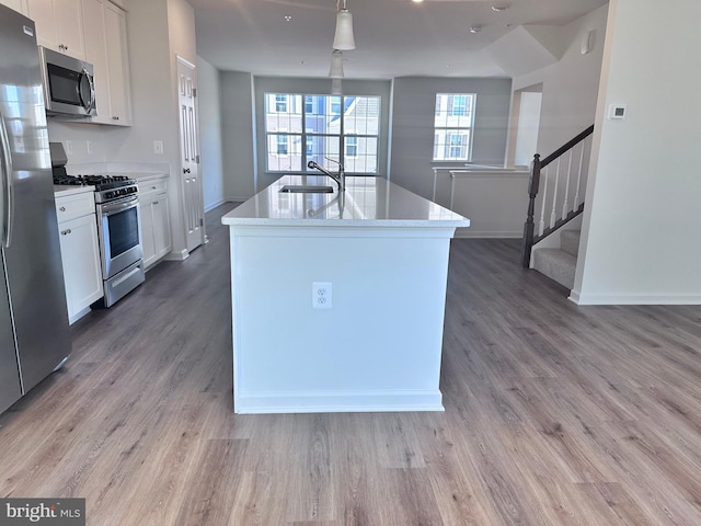 kitchen featuring sink, white cabinetry, appliances with stainless steel finishes, hardwood / wood-style flooring, and a kitchen island with sink