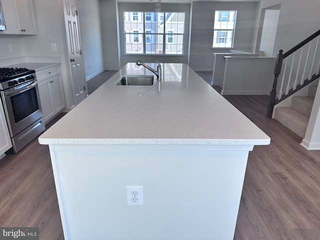 kitchen featuring white cabinetry, a kitchen island with sink, sink, and stainless steel gas range oven