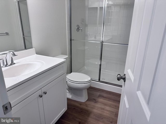 bathroom with hardwood / wood-style flooring, vanity, a shower with door, and toilet