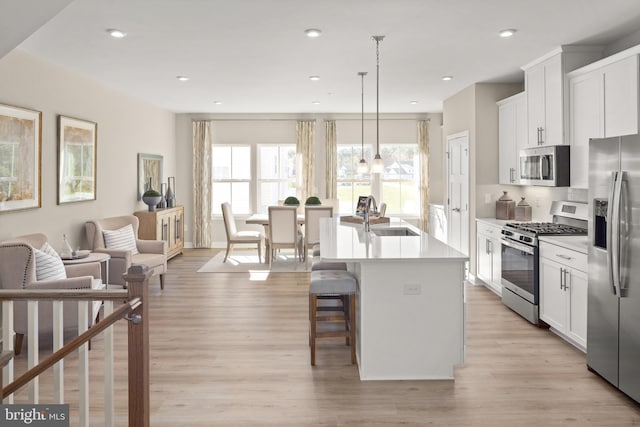 kitchen with sink, white cabinetry, decorative light fixtures, appliances with stainless steel finishes, and a kitchen island with sink