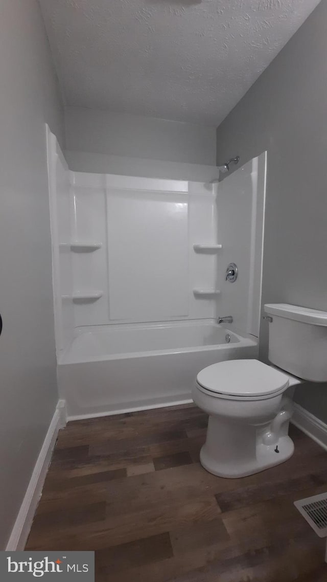 bathroom featuring shower / bathtub combination, wood-type flooring, toilet, and a textured ceiling