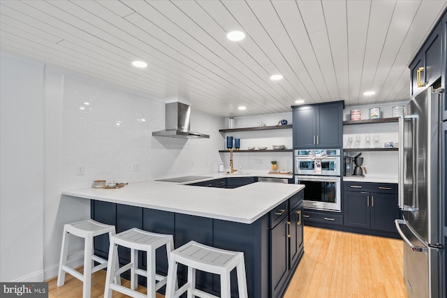 kitchen with appliances with stainless steel finishes, wall chimney exhaust hood, kitchen peninsula, and decorative backsplash