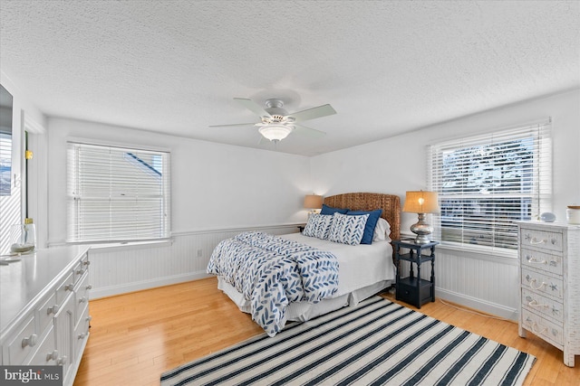 bedroom featuring ceiling fan, multiple windows, light hardwood / wood-style flooring, and a textured ceiling