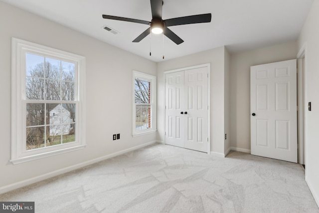 unfurnished bedroom featuring multiple windows, light colored carpet, a closet, and ceiling fan