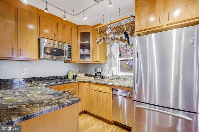 kitchen featuring stainless steel appliances, sink, light hardwood / wood-style flooring, and dark stone countertops